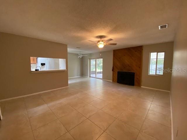 unfurnished living room with ceiling fan, a wealth of natural light, a fireplace, and light tile patterned floors