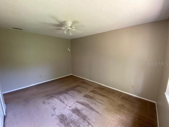 empty room featuring a textured ceiling, ceiling fan, and dark colored carpet