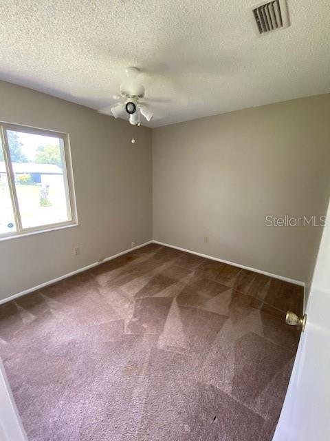 empty room featuring a textured ceiling, dark colored carpet, and ceiling fan