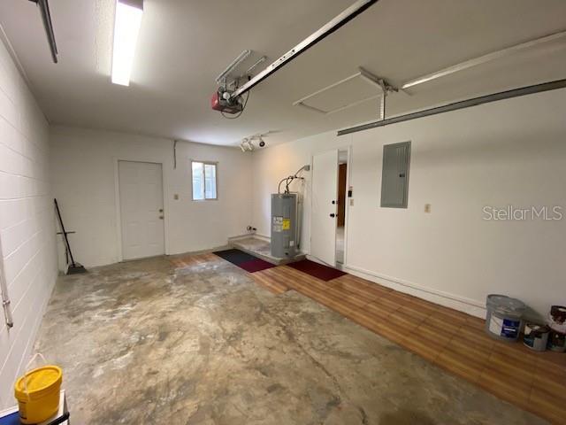 garage with electric panel, a garage door opener, and electric water heater