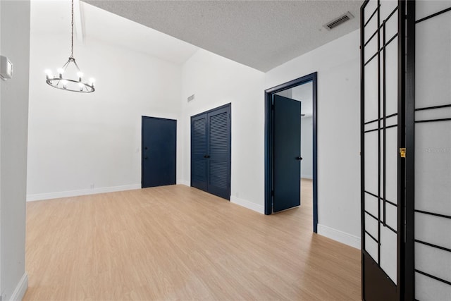 empty room with a notable chandelier, a textured ceiling, and light hardwood / wood-style floors