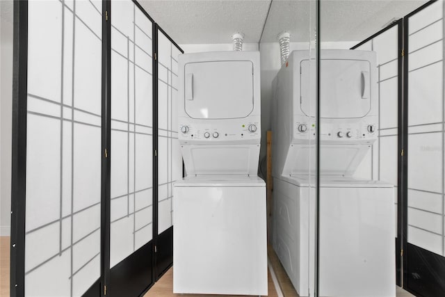 laundry area featuring a textured ceiling, stacked washer / drying machine, and light hardwood / wood-style floors