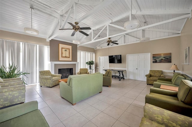 living room featuring ceiling fan, a glass covered fireplace, beam ceiling, and light tile patterned flooring