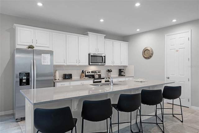 kitchen featuring white cabinets, stainless steel appliances, tasteful backsplash, and an island with sink