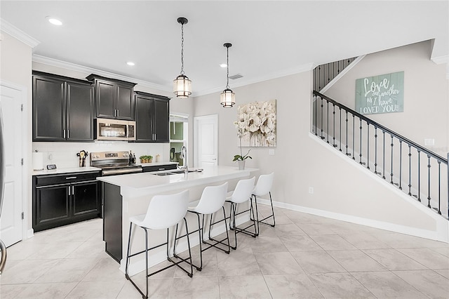 kitchen featuring crown molding, stainless steel appliances, sink, decorative light fixtures, and a center island with sink