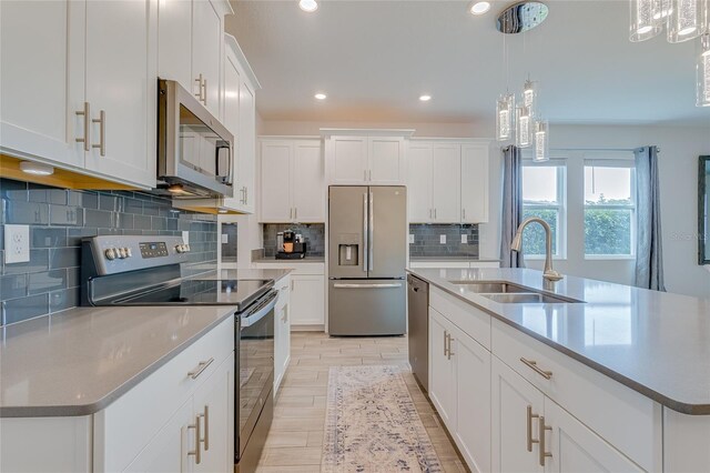 kitchen with white cabinetry, decorative backsplash, an island with sink, sink, and appliances with stainless steel finishes