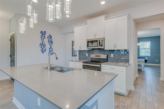 kitchen with appliances with stainless steel finishes, sink, hanging light fixtures, an island with sink, and white cabinetry