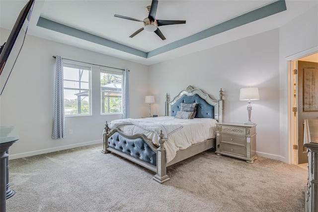 carpeted bedroom with ceiling fan and a raised ceiling