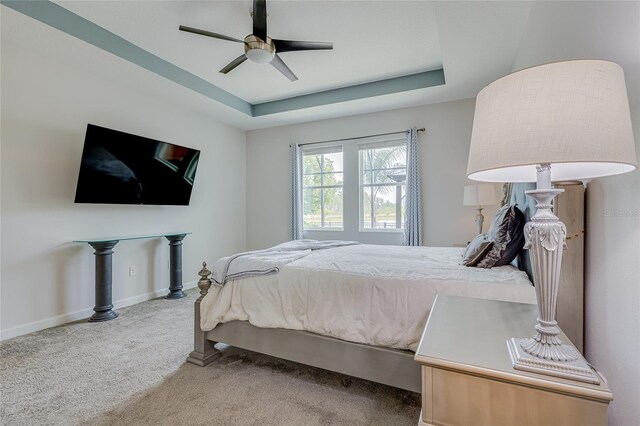 carpeted bedroom with a raised ceiling and ceiling fan