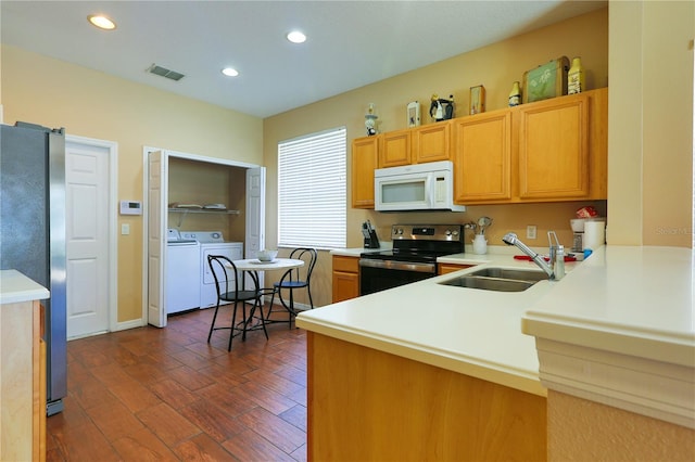 kitchen with sink, dark wood-type flooring, washer and clothes dryer, stainless steel appliances, and kitchen peninsula