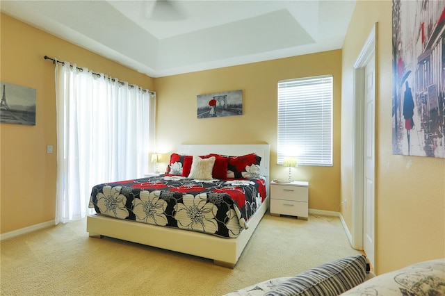 carpeted bedroom with a tray ceiling and multiple windows