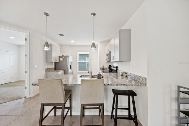 kitchen with decorative light fixtures, a breakfast bar area, light stone counters, kitchen peninsula, and stainless steel appliances