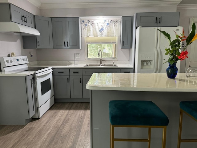 kitchen with a breakfast bar area, white appliances, a sink, light countertops, and gray cabinets