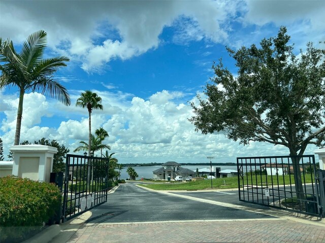 view of road featuring a gate, curbs, a water view, and a gated entry