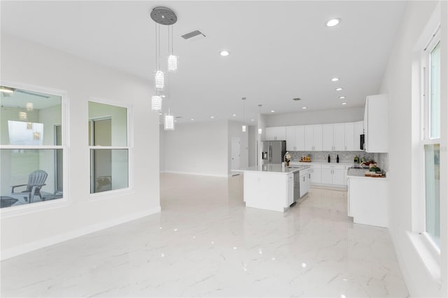 kitchen with hanging light fixtures, appliances with stainless steel finishes, a center island with sink, and white cabinets