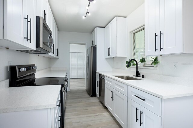 kitchen with stainless steel appliances, white cabinets, sink, light hardwood / wood-style floors, and track lighting