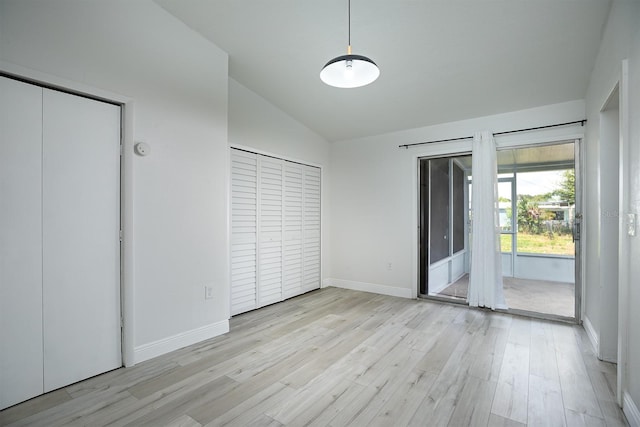 unfurnished bedroom with multiple closets, access to outside, vaulted ceiling, and light hardwood / wood-style flooring