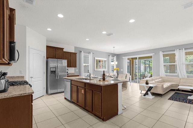 kitchen featuring pendant lighting, sink, stainless steel appliances, light stone counters, and a center island with sink