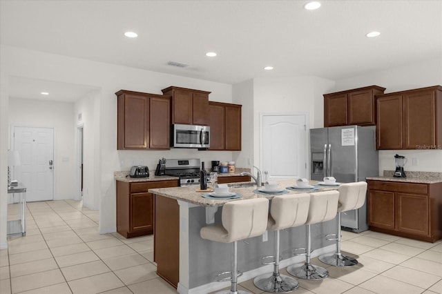 kitchen with light tile patterned floors, stainless steel appliances, an island with sink, and a breakfast bar