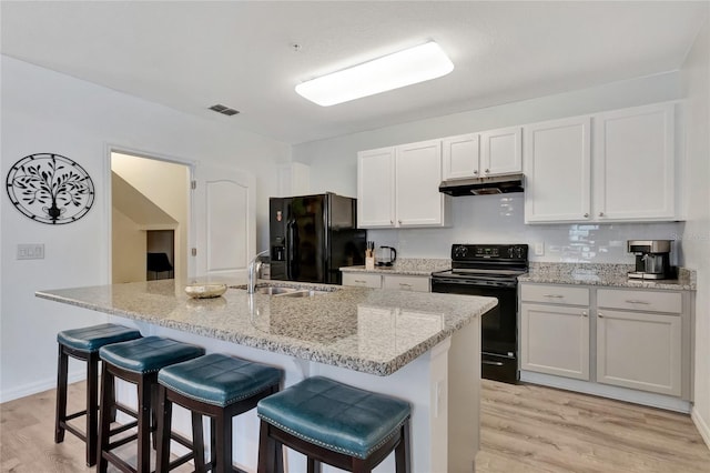 kitchen featuring a breakfast bar area, black appliances, sink, light hardwood / wood-style floors, and white cabinetry