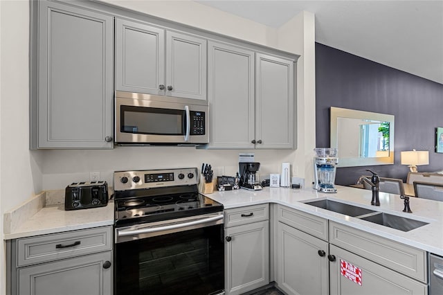 kitchen with sink, appliances with stainless steel finishes, light stone counters, and gray cabinets