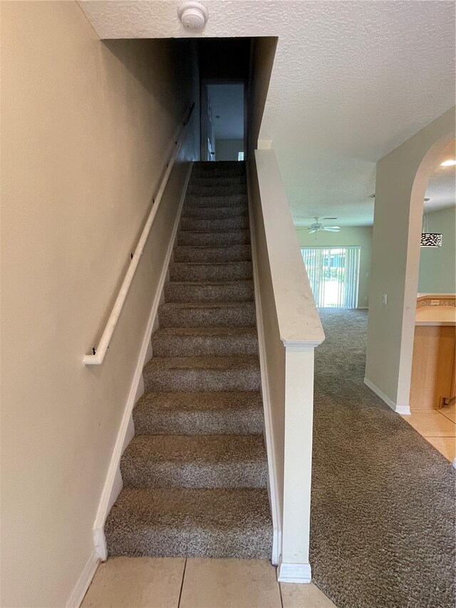 stairs featuring tile patterned flooring, a textured ceiling, and ceiling fan