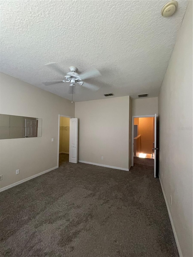 unfurnished bedroom with a spacious closet, a textured ceiling, ceiling fan, and dark colored carpet