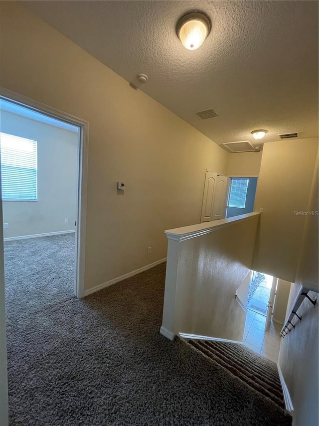 corridor featuring dark colored carpet and a textured ceiling