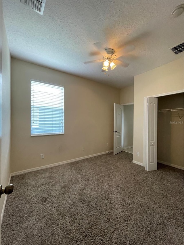 unfurnished bedroom with ceiling fan, a textured ceiling, dark carpet, and a closet