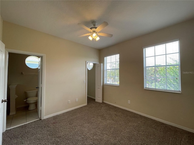 unfurnished bedroom with connected bathroom, dark carpet, a textured ceiling, and ceiling fan