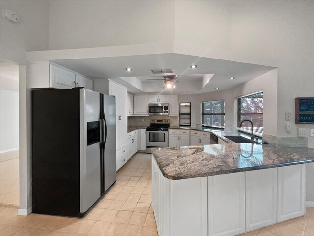 kitchen featuring white cabinetry, stainless steel appliances, kitchen peninsula, sink, and a raised ceiling