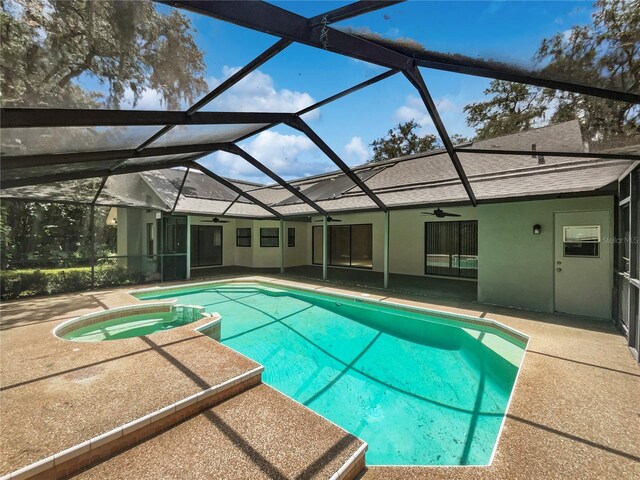 view of swimming pool featuring glass enclosure, ceiling fan, a patio, and an in ground hot tub