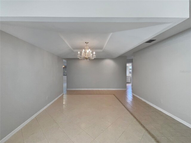 unfurnished room featuring a raised ceiling and a chandelier