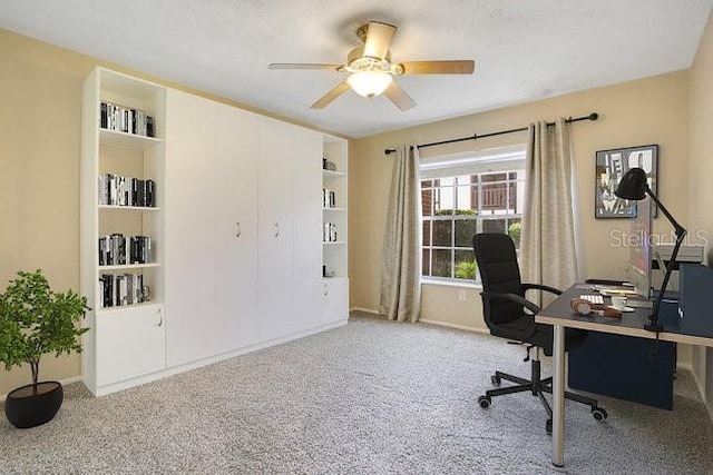 carpeted home office with ceiling fan and built in shelves