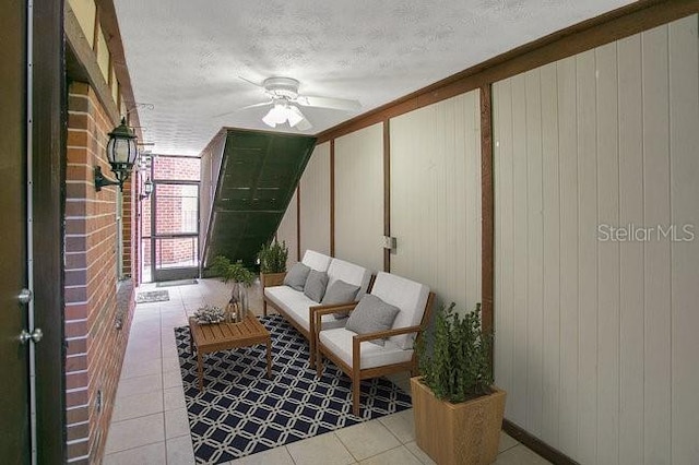 living area featuring light tile patterned flooring, ceiling fan, a textured ceiling, and wood walls