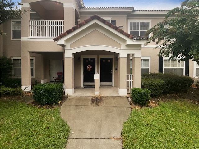 view of exterior entry featuring a balcony and a lawn