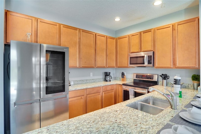 kitchen featuring sink, appliances with stainless steel finishes, a textured ceiling, and light stone counters