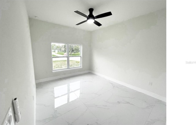 empty room with ceiling fan, marble finish floor, and baseboards