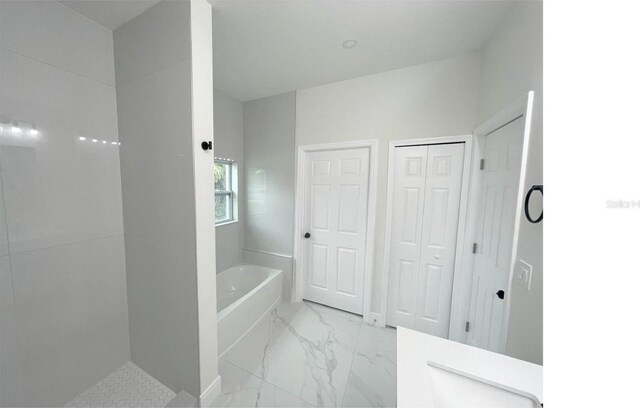 bathroom featuring marble finish floor and a bath