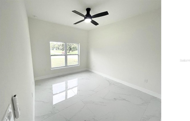 empty room with a ceiling fan, marble finish floor, and baseboards