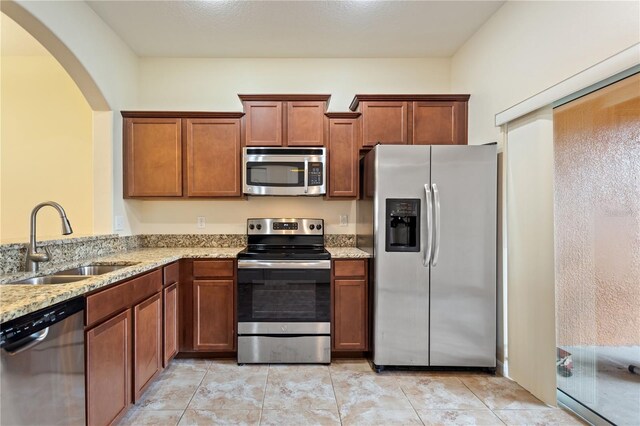 kitchen with appliances with stainless steel finishes, sink, light tile patterned floors, and light stone countertops