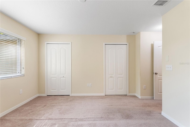 unfurnished bedroom featuring multiple closets and light carpet