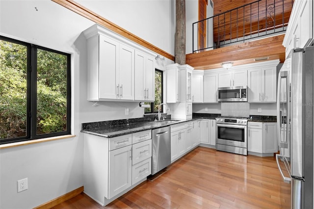 kitchen featuring white cabinets, a towering ceiling, stainless steel appliances, light wood-style floors, and a sink