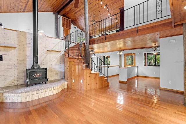 unfurnished living room featuring high vaulted ceiling, stairway, wooden ceiling, and a wood stove