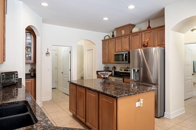 kitchen featuring dark stone countertops, light tile patterned floors, a center island, and appliances with stainless steel finishes