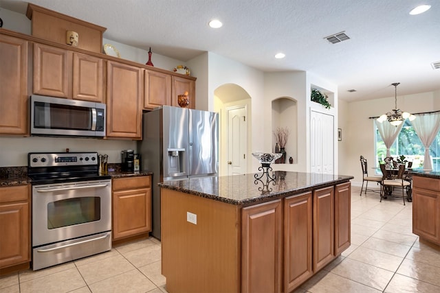 kitchen with decorative light fixtures, stainless steel appliances, dark stone counters, and a kitchen island