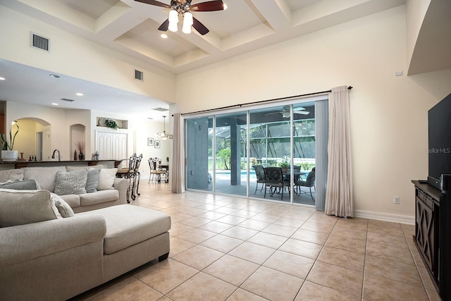 living room featuring coffered ceiling, light tile patterned flooring, ceiling fan, and a high ceiling