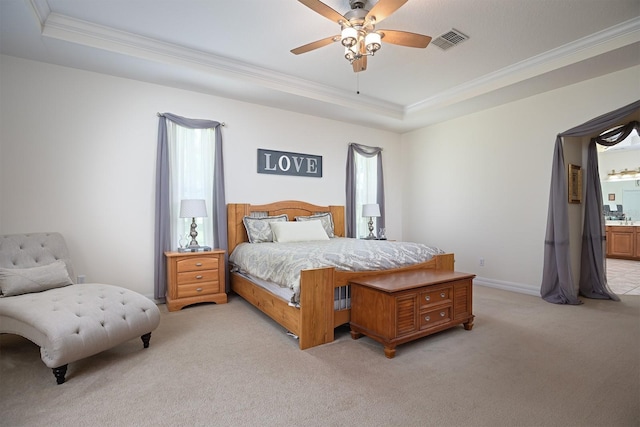 bedroom with ceiling fan, connected bathroom, ornamental molding, light colored carpet, and a raised ceiling