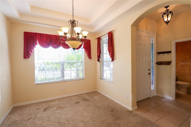 tiled spare room featuring a raised ceiling, a wealth of natural light, and an inviting chandelier