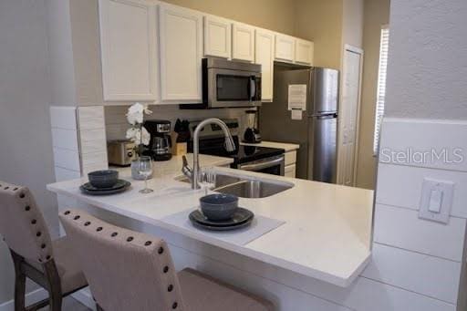 kitchen featuring sink, a breakfast bar area, stainless steel appliances, white cabinets, and kitchen peninsula